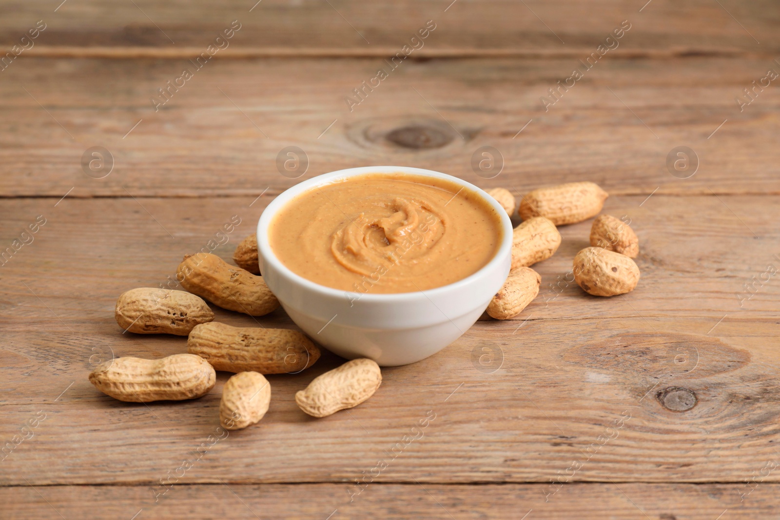 Photo of Delicious nut butter in bowl and peanuts on wooden table