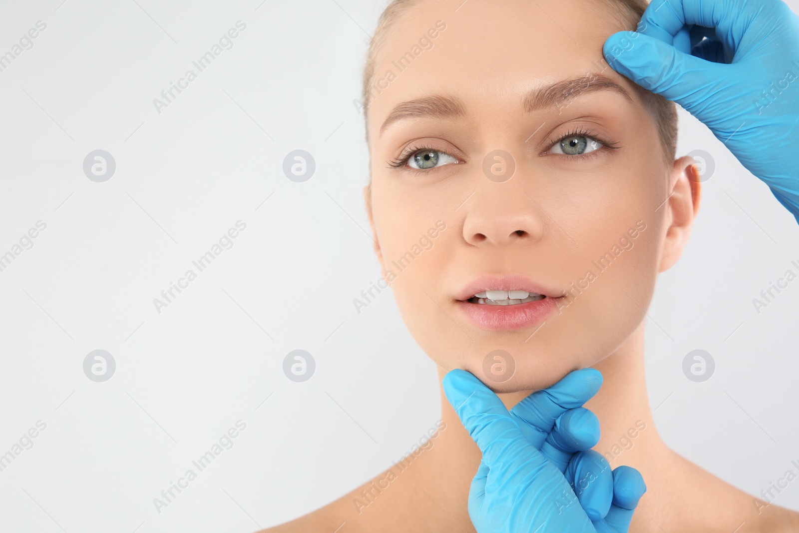 Photo of Doctor examining young woman face before cosmetic surgery on white background