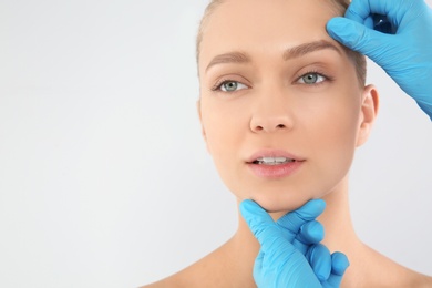 Photo of Doctor examining young woman face before cosmetic surgery on white background