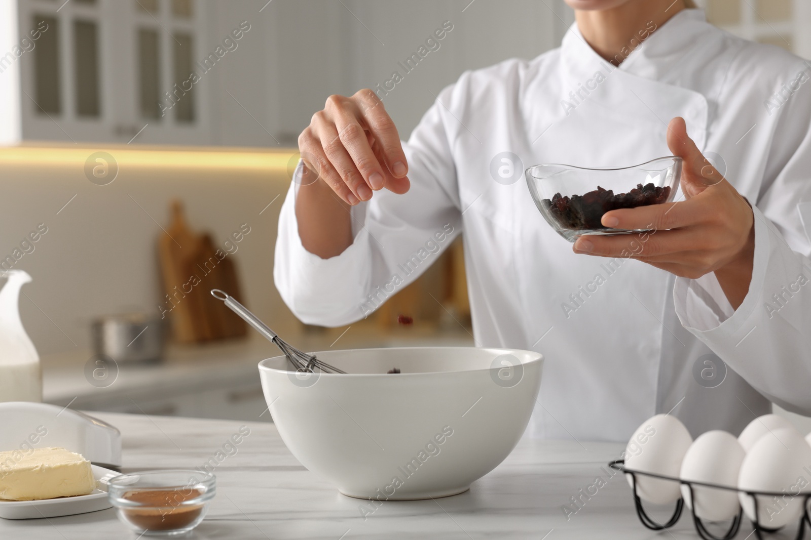 Photo of Professional chef adding raisins into dough at white marble table indoors, closeup