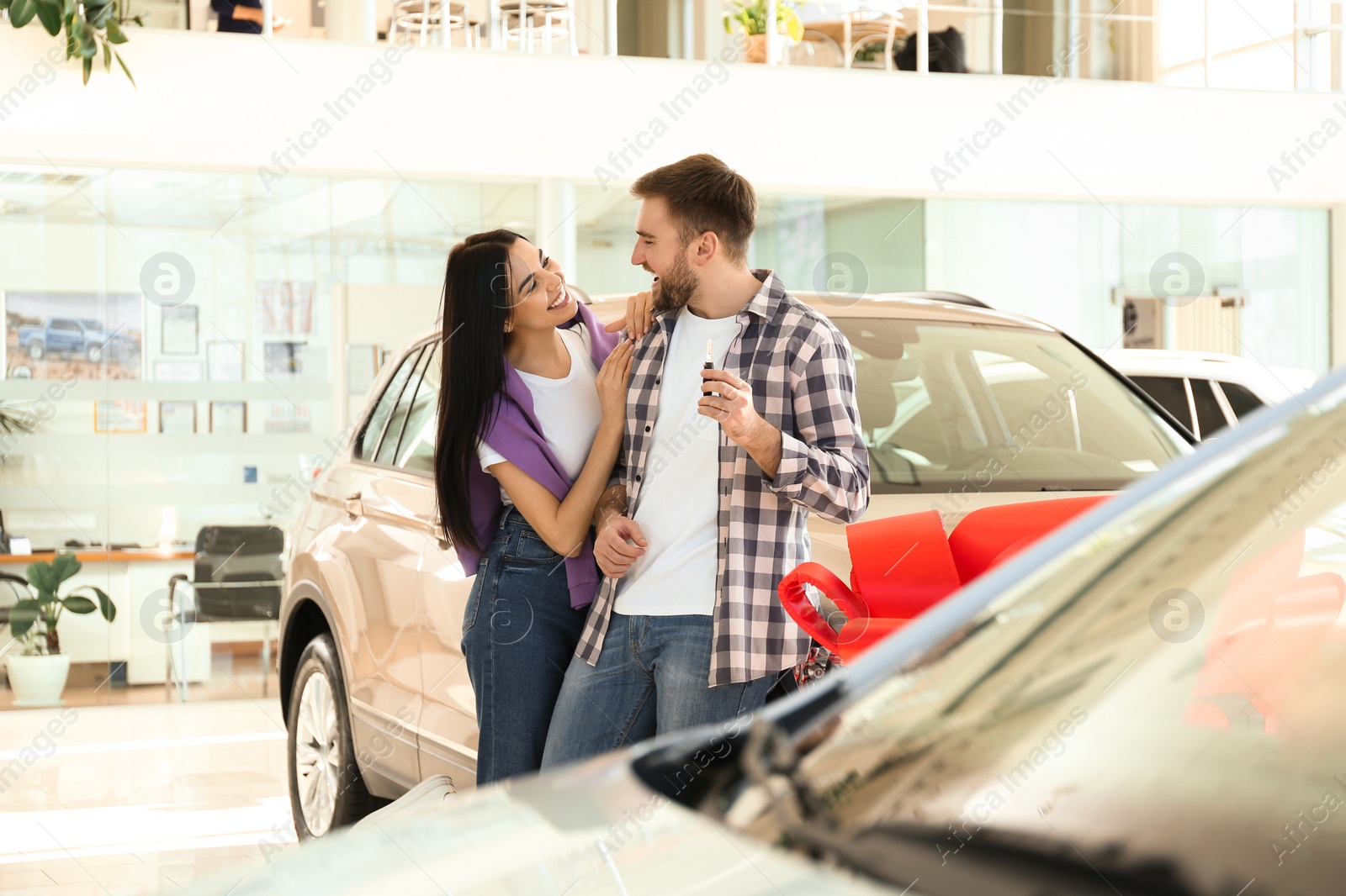 Photo of Happy couple with car key in modern auto dealership