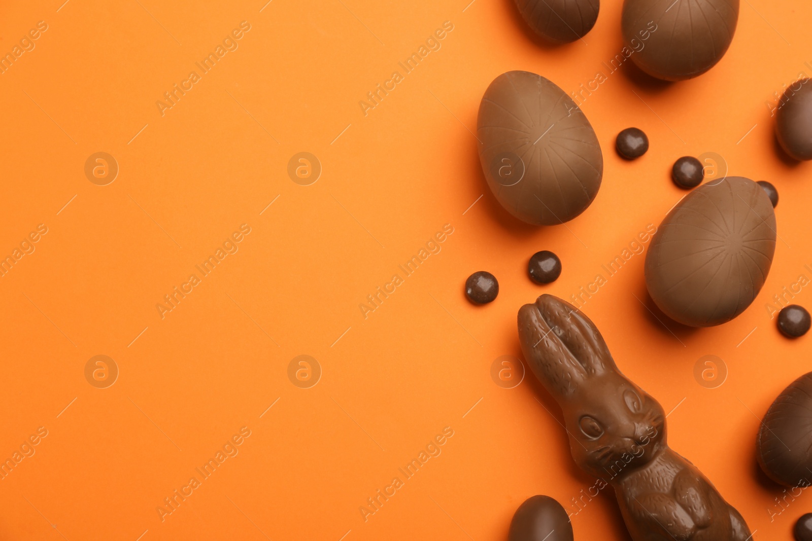 Photo of Sweet chocolate eggs and bunny on orange background, flat lay. Space for text