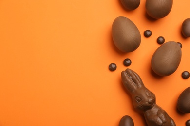 Sweet chocolate eggs and bunny on orange background, flat lay. Space for text