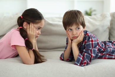 Upset brother and sister on sofa at home