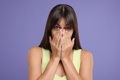 Embarrassed woman covering mouth with hands on violet background