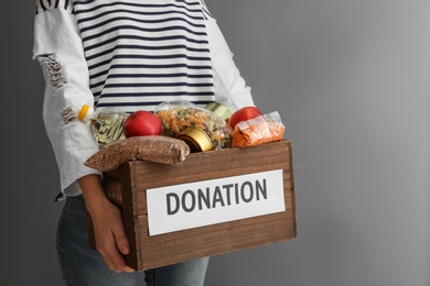 Photo of Woman holding donation box with food on gray background, closeup