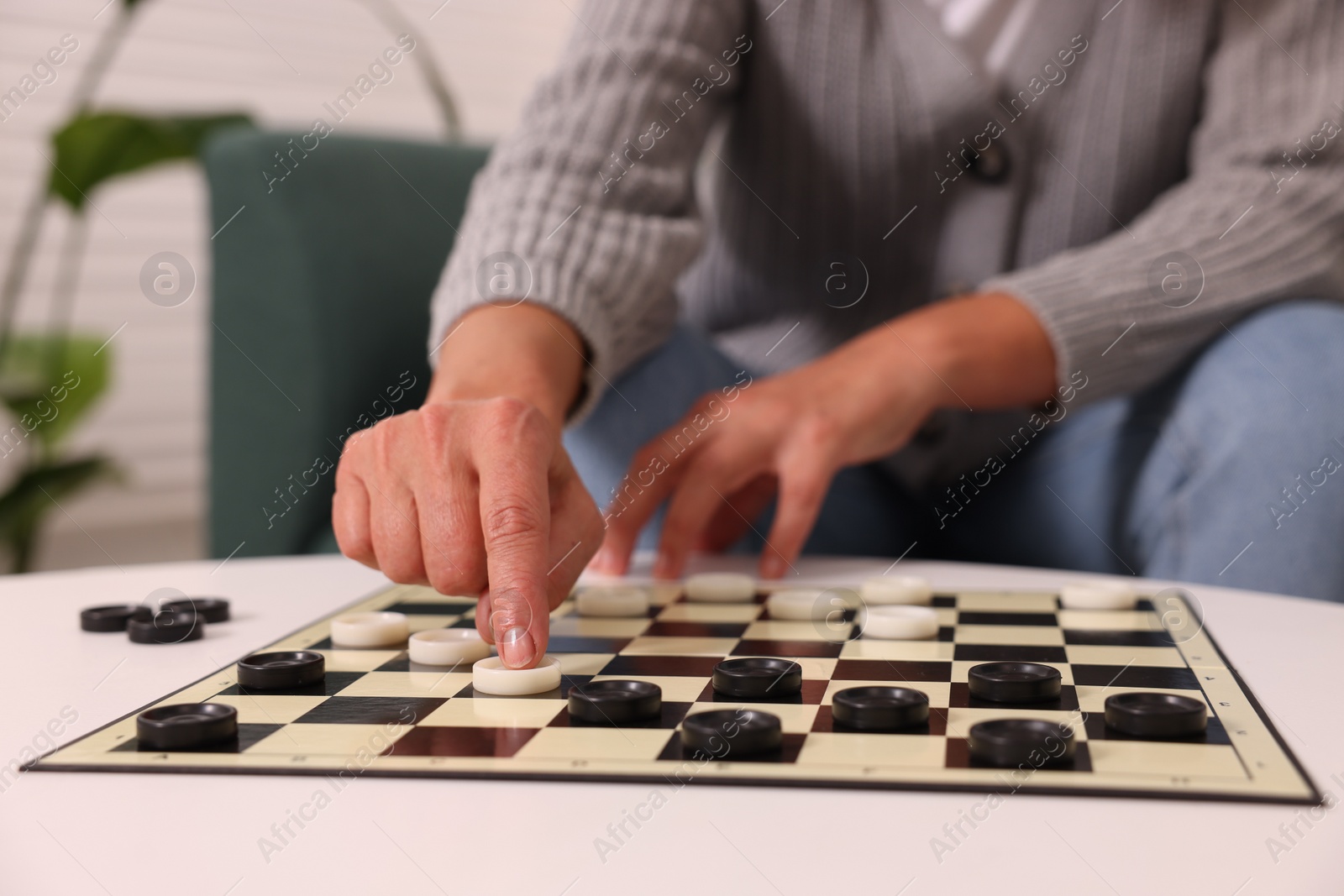 Photo of Woman playing checkers at white table indoors, closeup