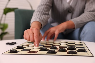 Photo of Woman playing checkers at white table indoors, closeup