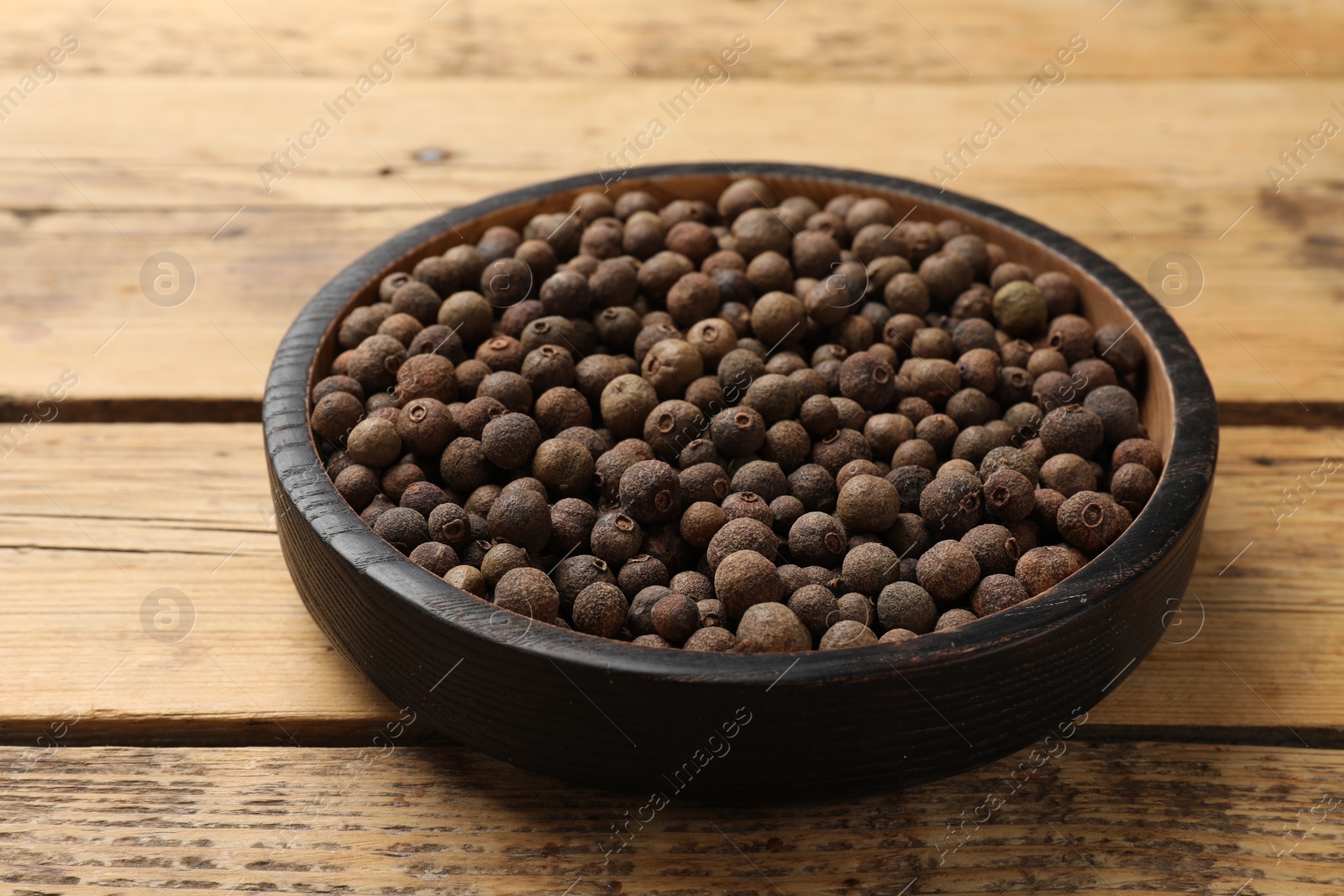 Photo of Aromatic allspice pepper grains in bowl on wooden table, closeup