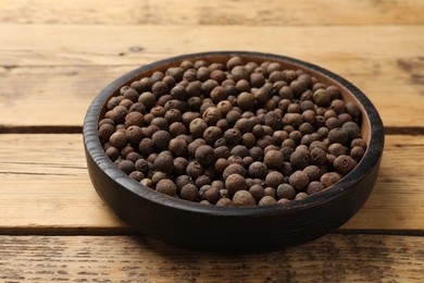 Photo of Aromatic allspice pepper grains in bowl on wooden table, closeup