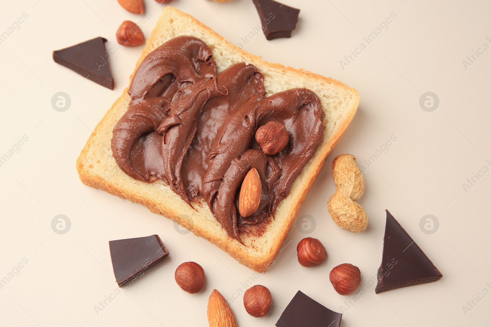 Photo of Tasty toast with chocolate paste and nuts on beige background, flat lay