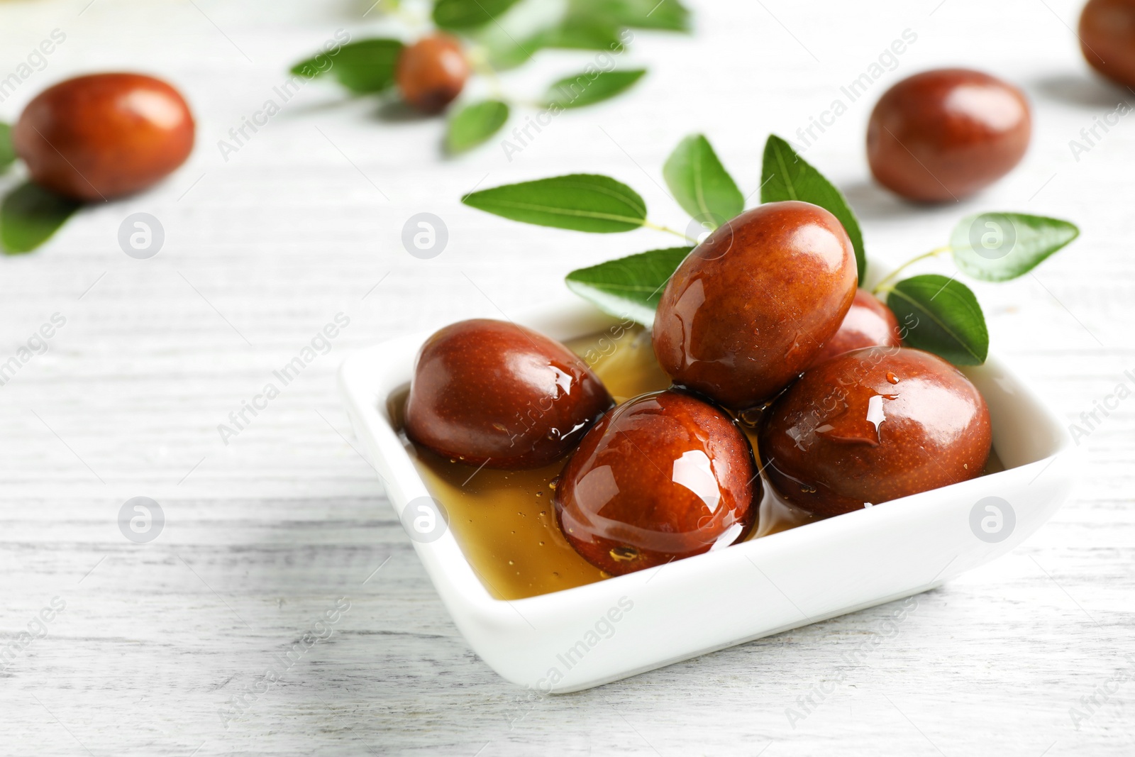 Photo of Sauce boat with jojoba oil and seeds on white wooden table