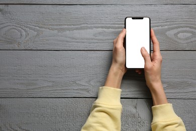 Woman with smartphone at grey wooden table, top view. Space for text