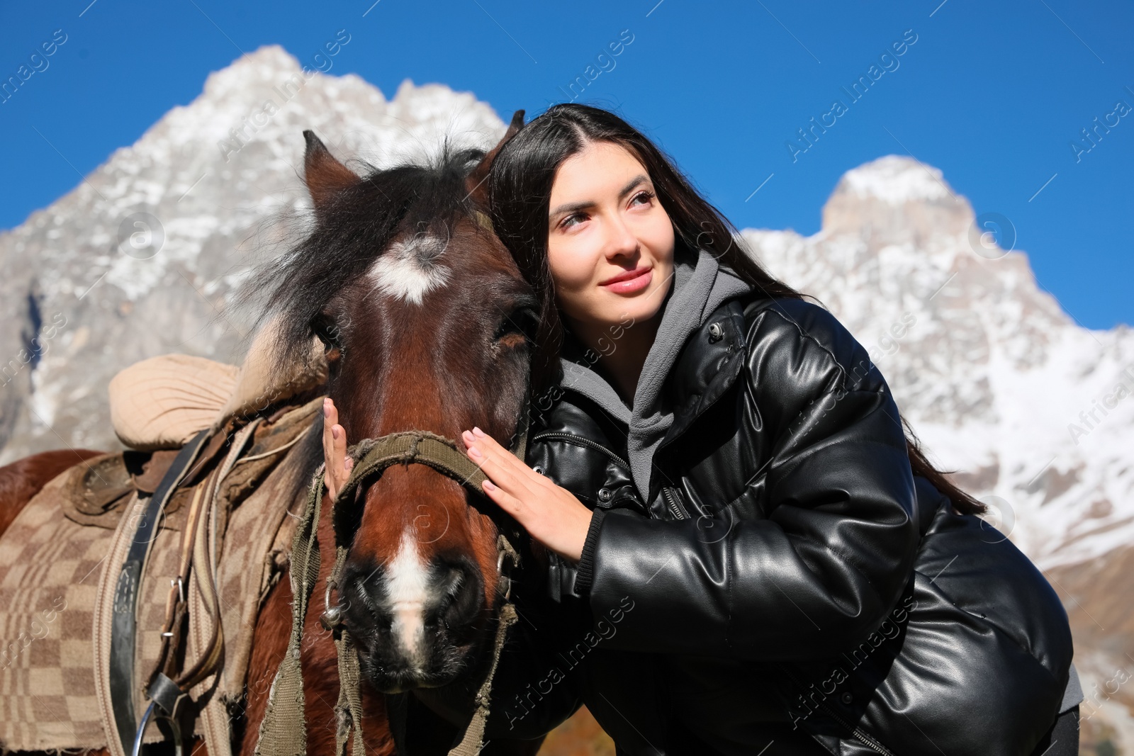 Photo of Young woman hugging horse in mountains on sunny day. Beautiful pet