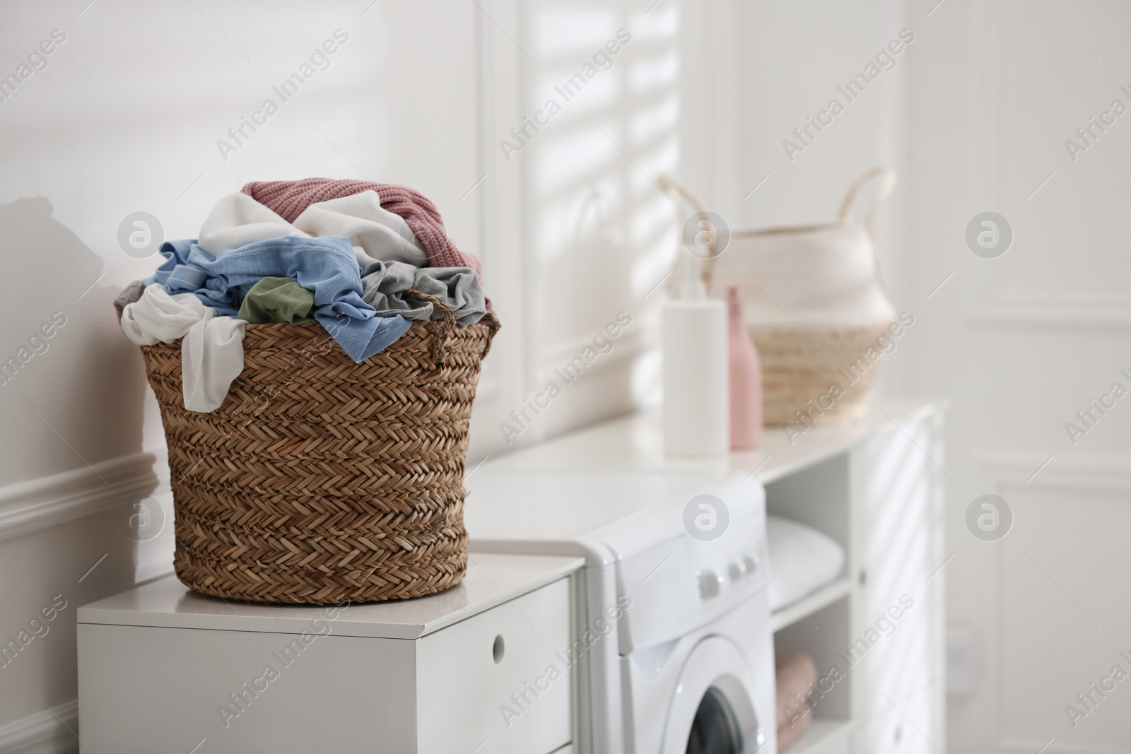 Photo of Wicker basket with dirty laundry on washing machine indoors, space for text