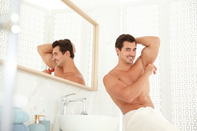 Handsome young man applying deodorant in bathroom