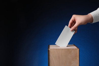 Photo of Woman putting her vote into ballot box on dark blue background, closeup. Space for text