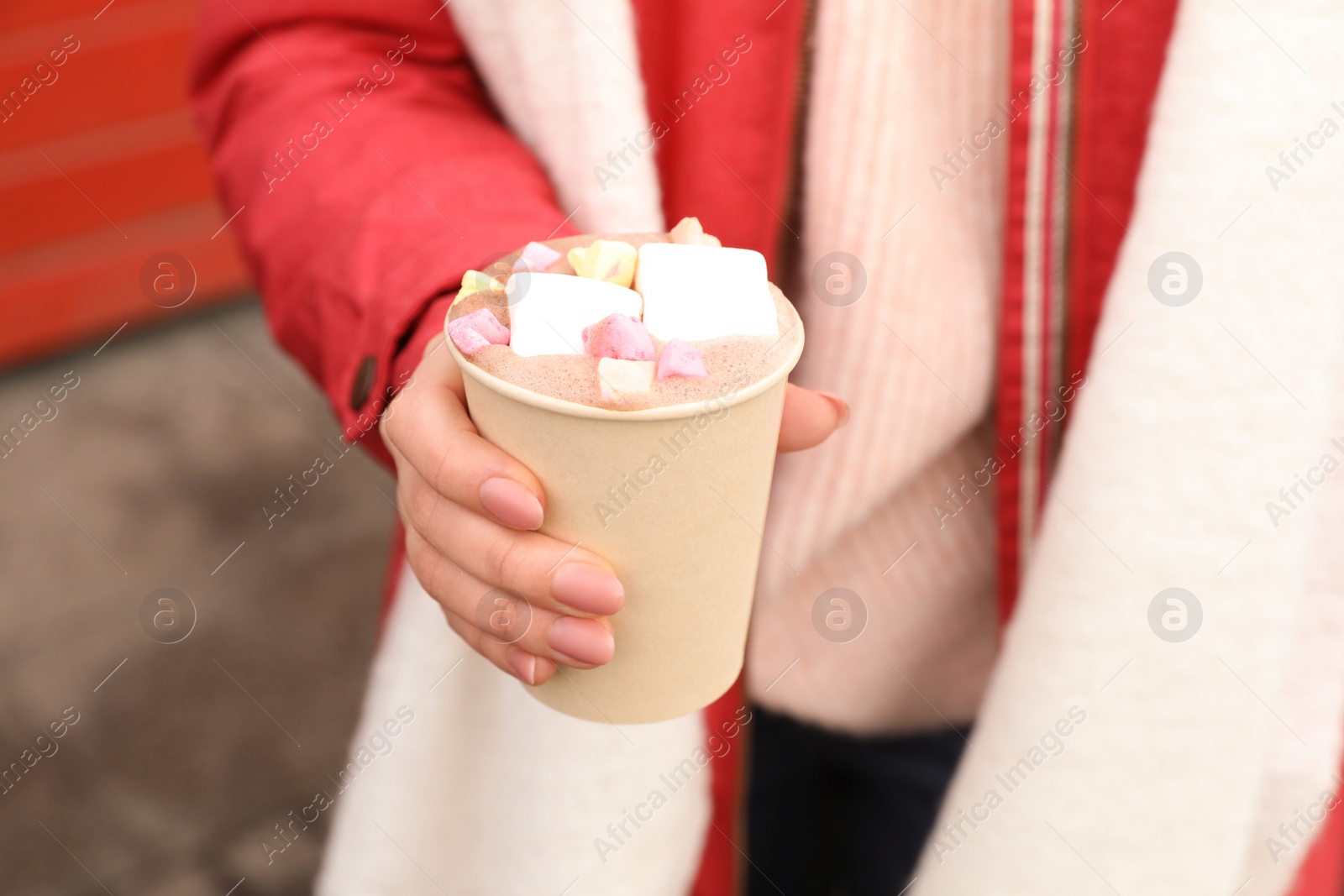 Photo of Woman holding warm drink with marshmallows outdoors, closeup