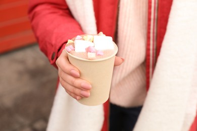 Woman holding warm drink with marshmallows outdoors, closeup