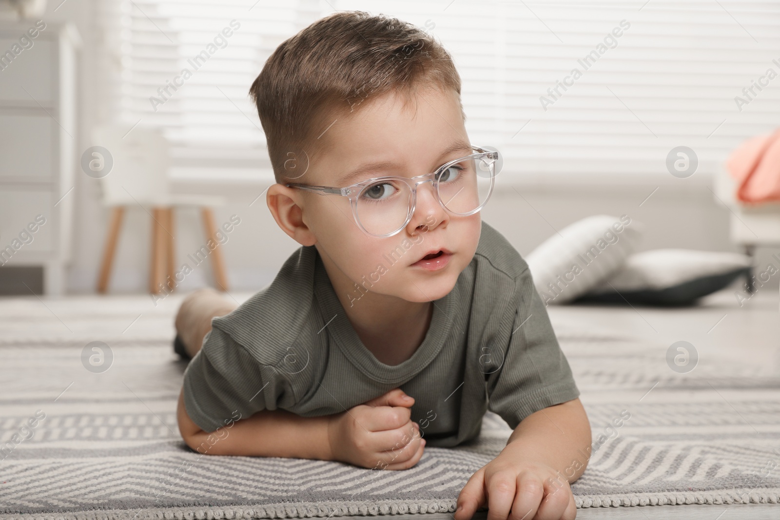 Photo of Cute little boy in glasses on floor at home