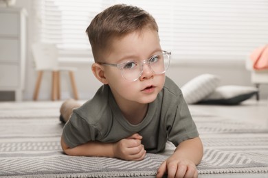 Photo of Cute little boy in glasses on floor at home