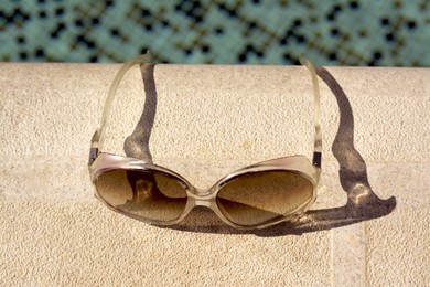 Stylish sunglasses near outdoor swimming pool on sunny day