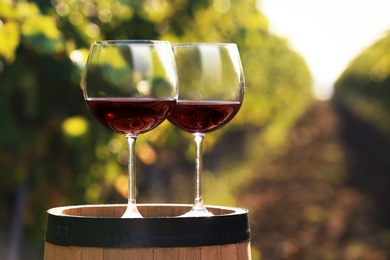 Photo of Glasses with red wine on barrel outdoors. Space for text