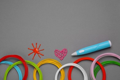 Photo of Stylish 3D pen, colorful plastic filaments and different figures on gray background, flat lay. Space for text