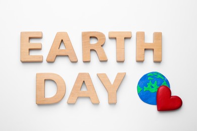 Photo of Phrase Earth Day of wooden letters and red heart with planet model on white background, top view