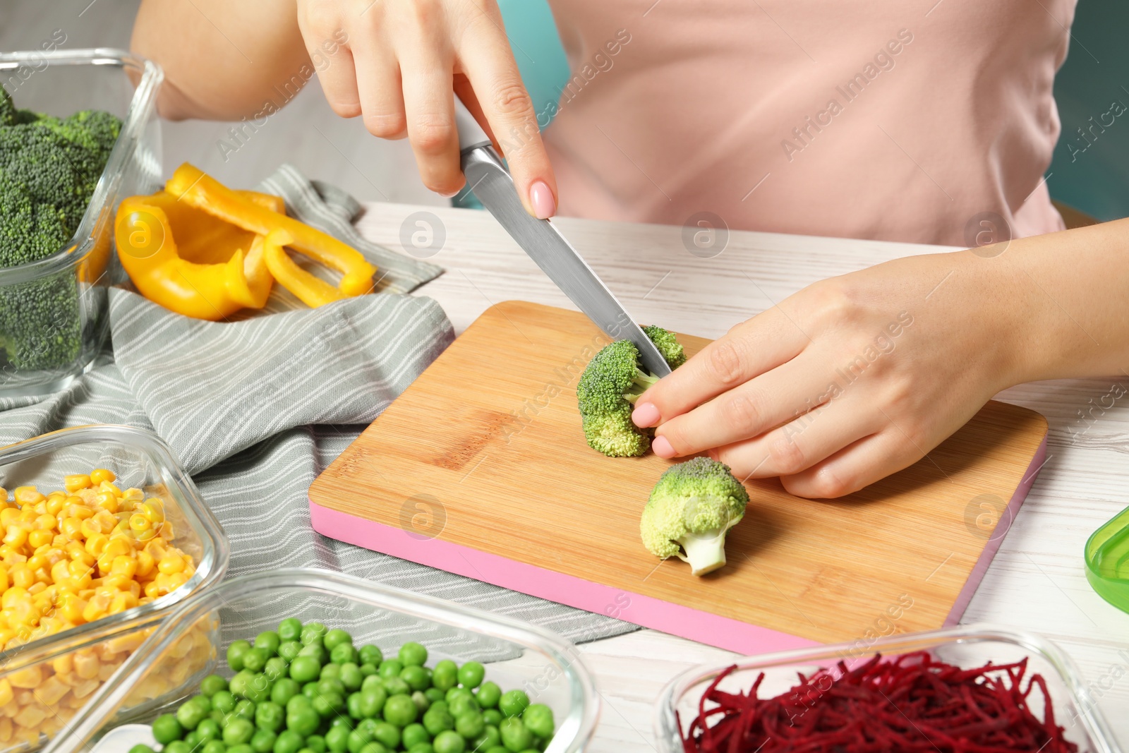 Photo of Woman cutting broccoli and glass containers with fresh products on white wooden table, closeup. Food storage