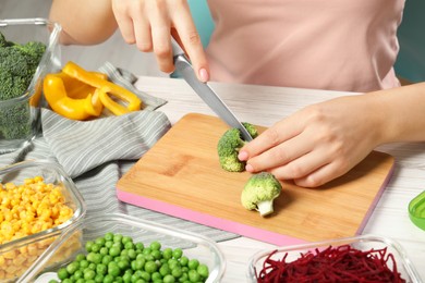 Photo of Woman cutting broccoli and glass containers with fresh products on white wooden table, closeup. Food storage