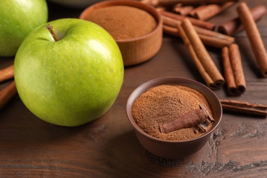 Photo of Fresh apple with cinnamon sticks and powder on wooden table