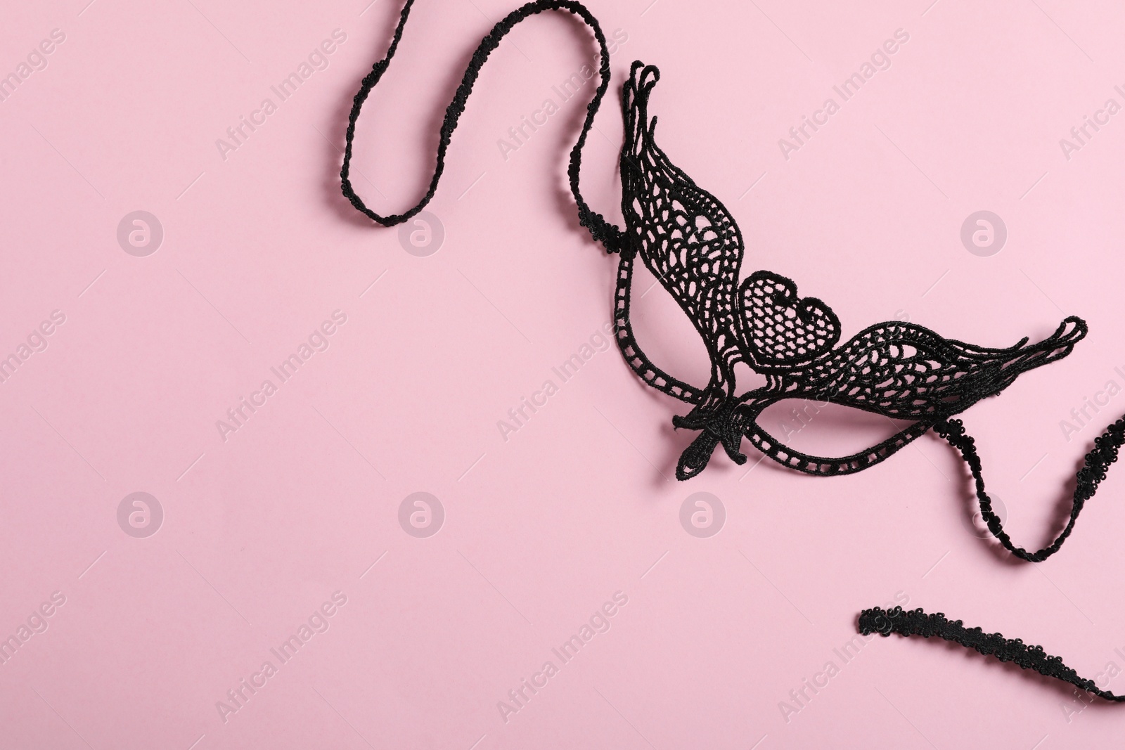 Photo of Black lace mask for sexual role play on pink background, top view with space for text