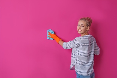 Photo of Woman in gloves cleaning color wall with rag