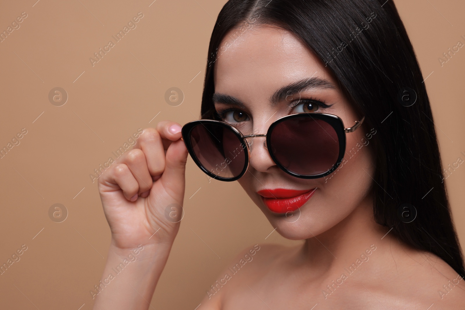 Photo of Attractive woman wearing fashionable sunglasses against beige background, closeup