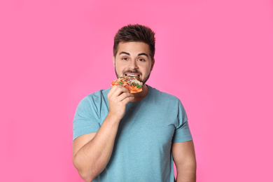 Handsome man eating pizza on pink background