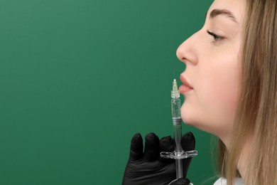 Photo of Cosmetologist with syringe on green background, closeup. Space for text