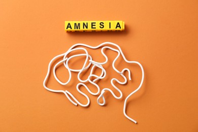 Photo of Word Amnesia and brain made of wires on orange background, flat lay