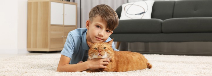 Image of Little boy with cute ginger cat on soft carpet at home. Banner design