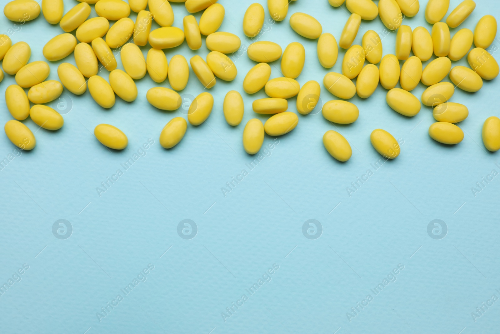 Photo of Many yellow dragee candies on light blue background, flat lay. Space for text