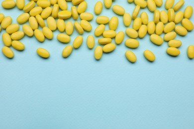 Photo of Many yellow dragee candies on light blue background, flat lay. Space for text