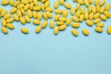 Many yellow dragee candies on light blue background, flat lay. Space for text