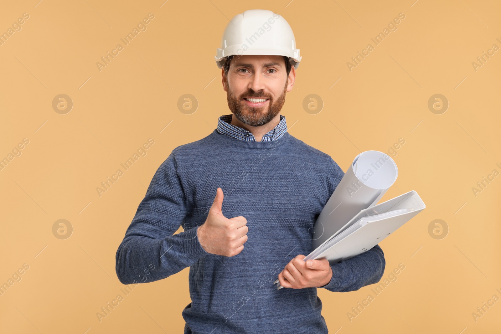 Photo of Architect in hard hat with draft and folder showing thumbs up on beige background