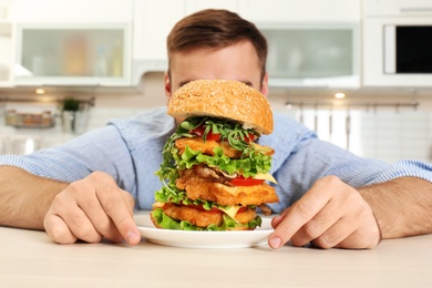 Hungry man and huge burger in kitchen