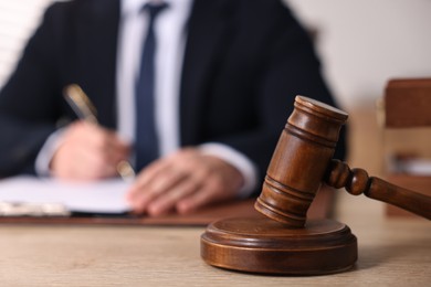 Photo of Notary writing notes at wooden table in office, focus on gavel