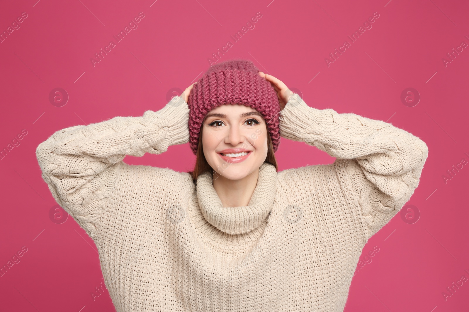 Photo of Young woman wearing warm sweater and hat on crimson background. Winter season