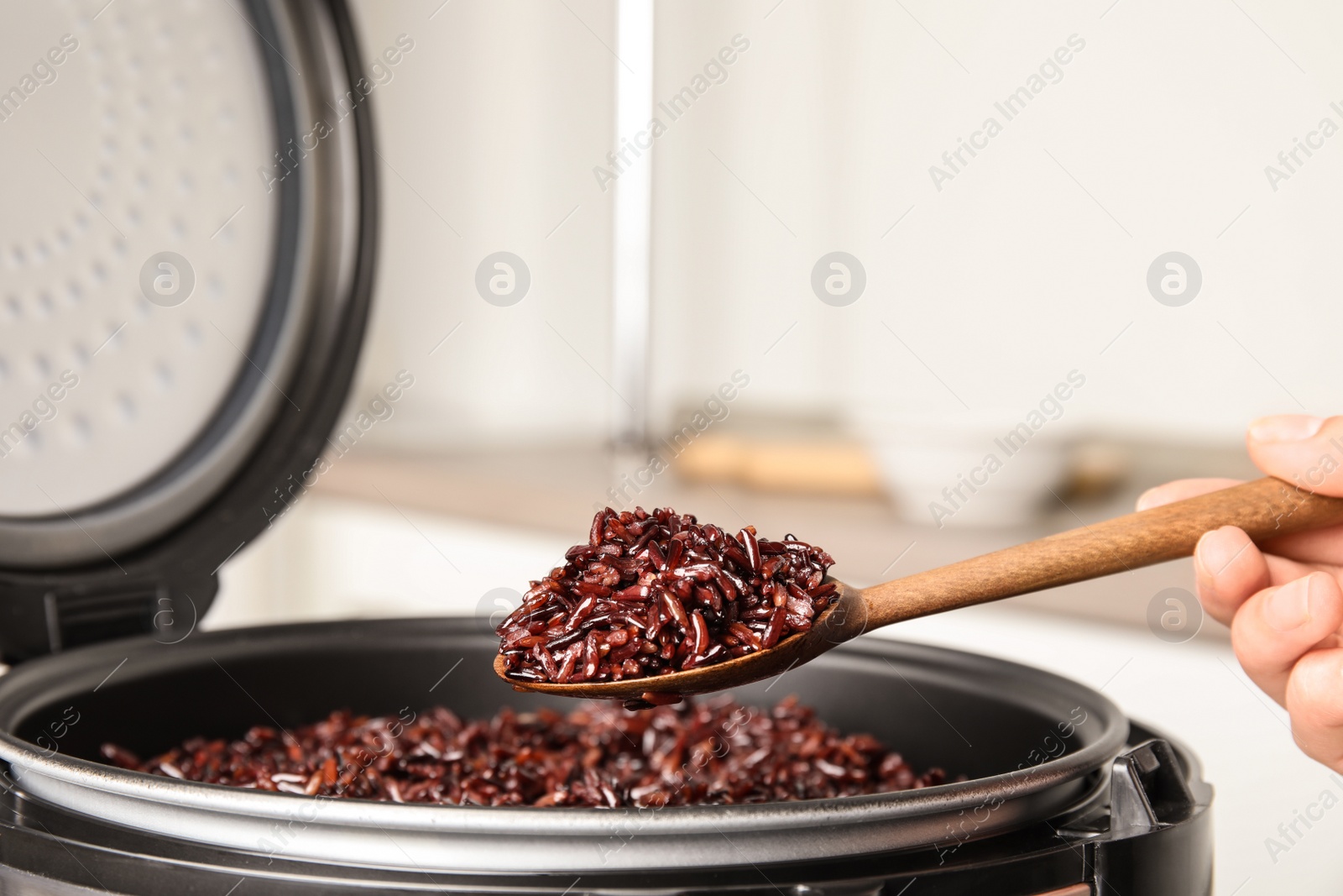 Photo of Woman taking delicious brown rice from multi cooker indoors, closeup