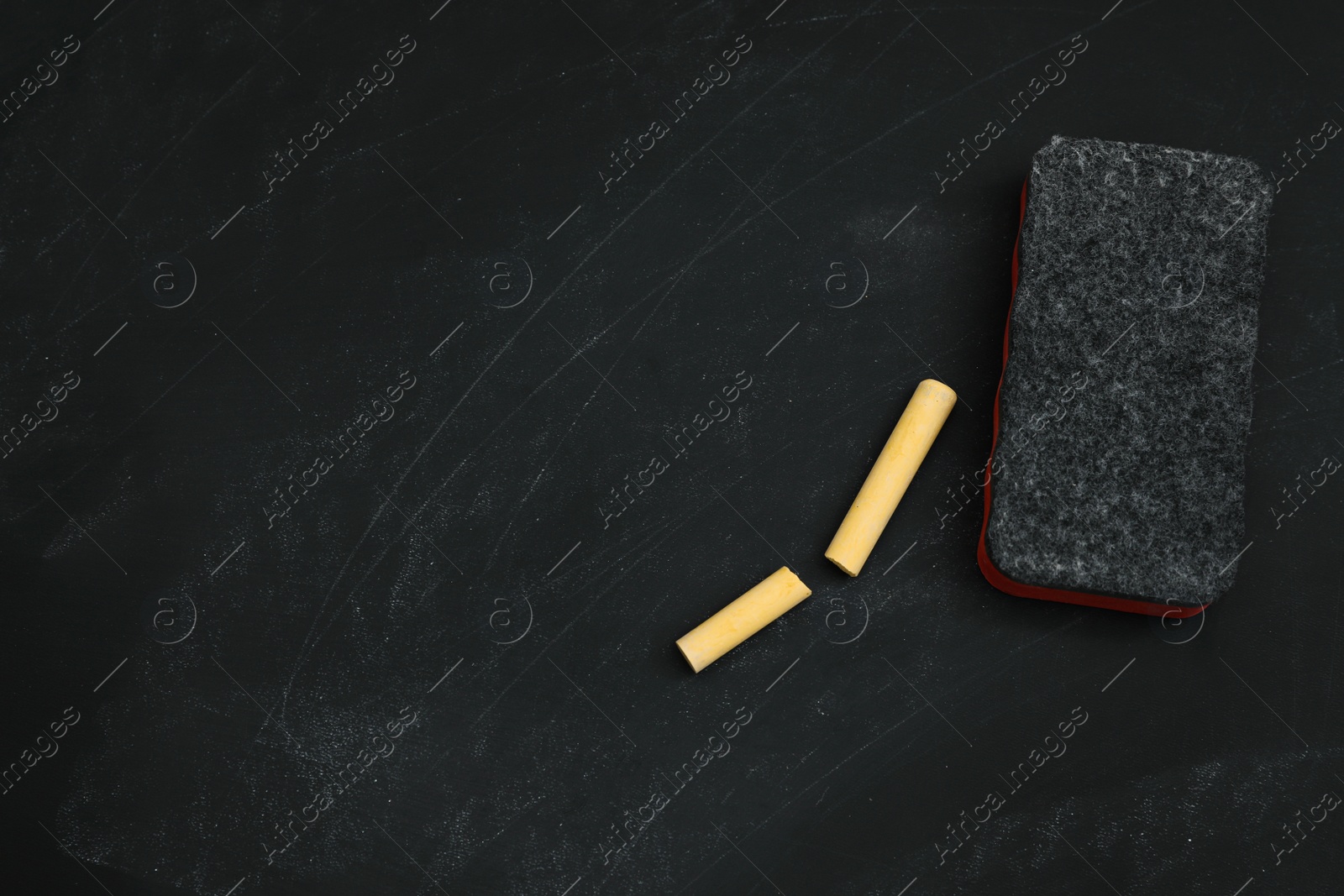 Photo of Pieces of yellow chalk and duster on black board, flat lay. Space for text