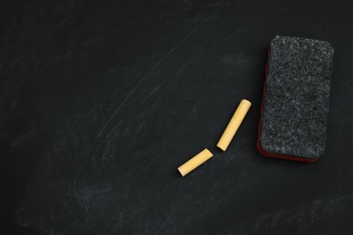 Pieces of yellow chalk and duster on black board, flat lay. Space for text