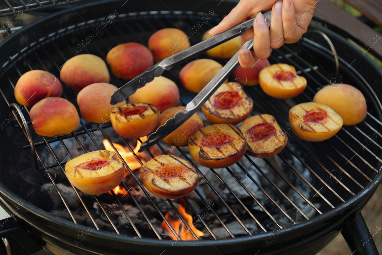 Photo of Woman cooking tasty peaches on grill, closeup